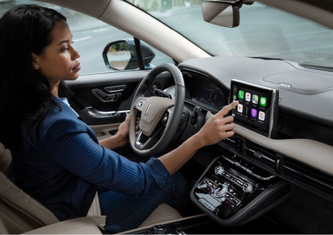 A woman in the driver’s seat of a 2022 Lincoln Corsair is touching the center digital screen to connect to Apple CarPlay<sup>®</sup> | Mark Ficken Lincoln in Charlotte NC