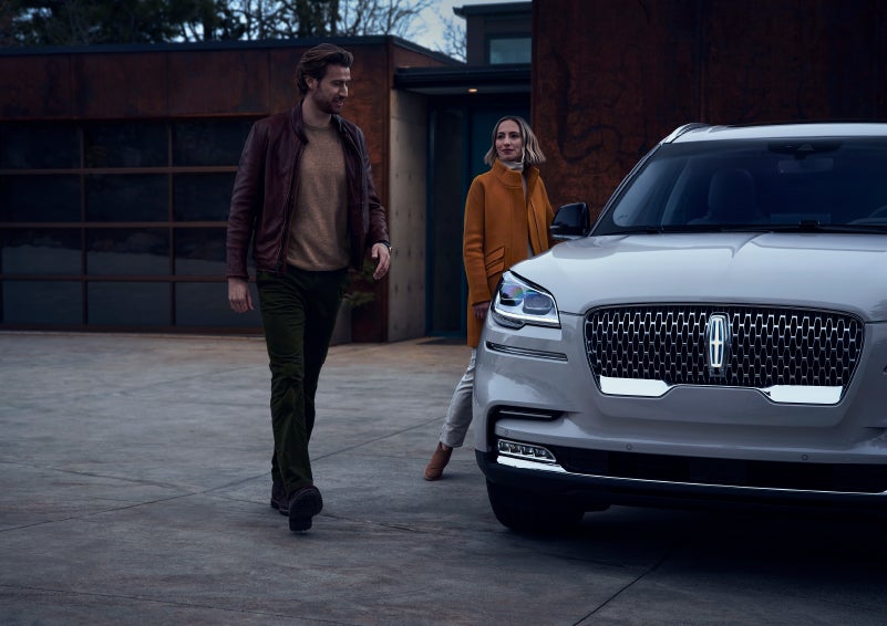 A man and a woman approaching a 2024 Lincoln Aviator® SUV, which illuminates certain lights when they are close | Mark Ficken Lincoln in Charlotte NC