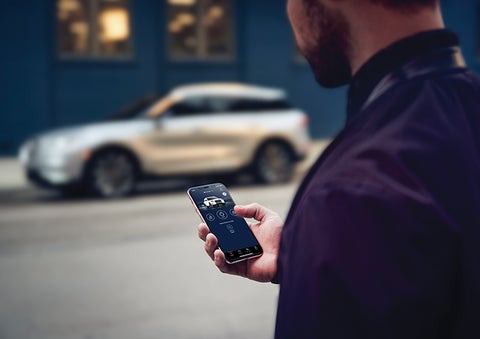 A person is shown interacting with a smartphone to connect to a Lincoln vehicle across the street. | Mark Ficken Lincoln in Charlotte NC